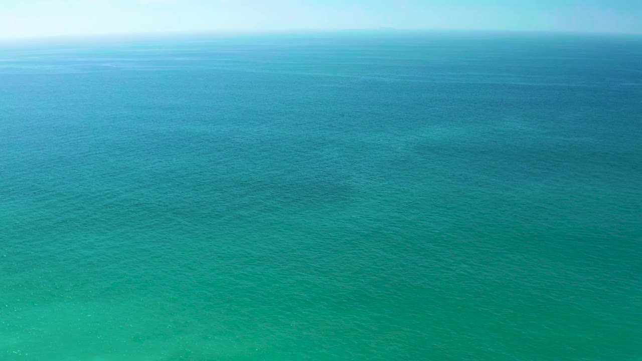 Blue-green ocean water with a soft horizon and faint seabed patches.