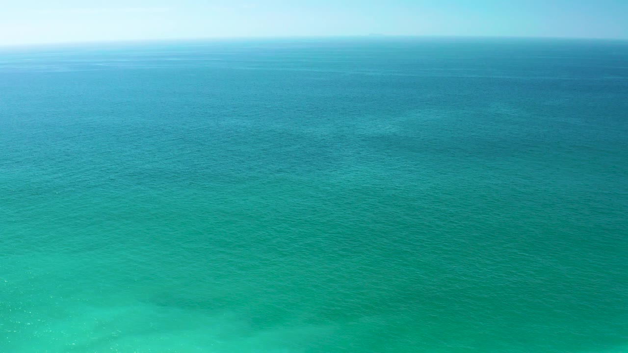Opening frame of turquoise ocean at Dreams Los Cabos, with darker blue water near the horizon, lighter shallow water below, pale sky above, and no visible people.