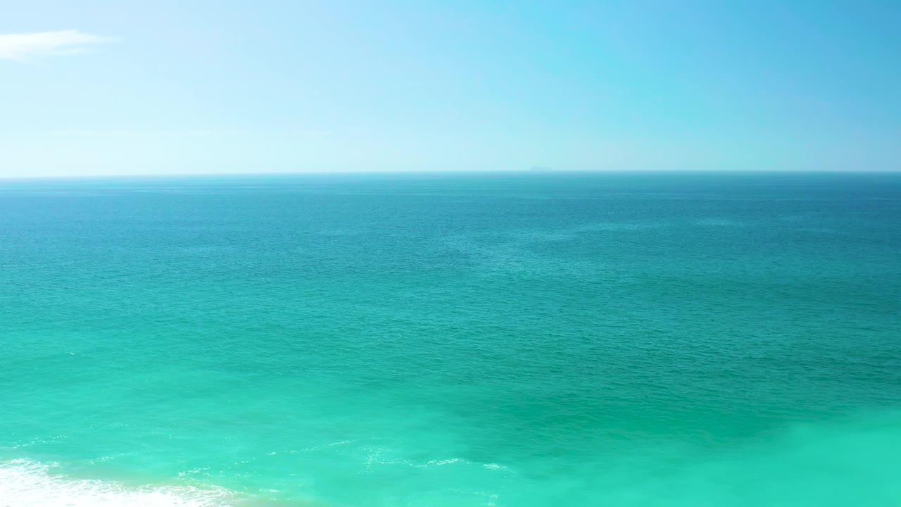 The second frame holds on the open Dreams Los Cabos coastline, showing deep blue water fading into turquoise shallows with a small white surf line and no visible people.