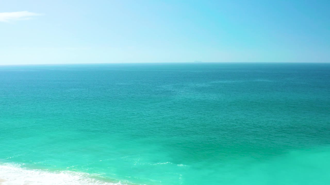 A wide view of the Dreams Los Cabos shore shows the horizon across the upper frame, open blue water in the center, turquoise surf below, and no visible people.