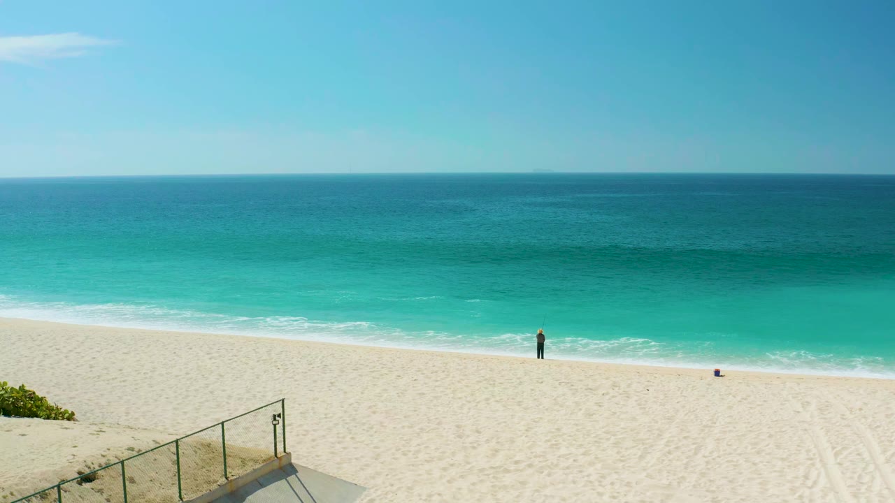 Elevated sandy beach and ocean view with railing and a distant beachgoer.