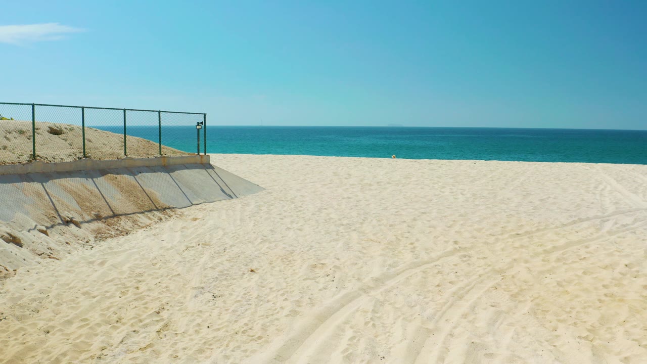 At Dreams Los Cabos in Baja California Sur, a wide frame keeps the concrete ramp and metal railing on the left edge, pale sand through the center, ocean on the horizon, and no visible people.