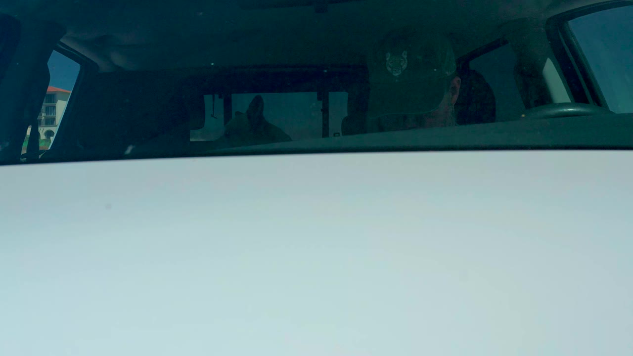 At Dreams Los Cabos in Baja California Sur, a white vehicle is viewed from outside through dark tinted glass as the driver sits partly obscured in the dim interior.