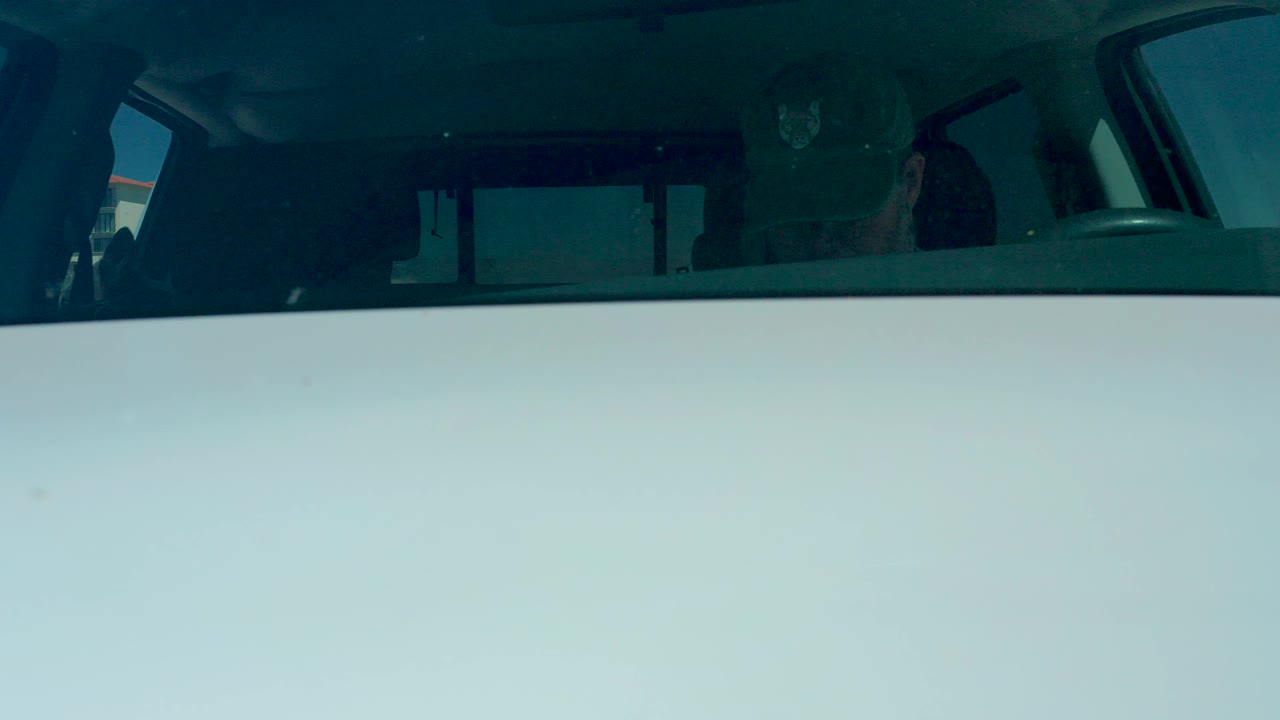 Opening view through the SUV windshield at Dreams Los Cabos, with dark occupant silhouettes inside the vehicle and the bright exterior reflected across the glass.
