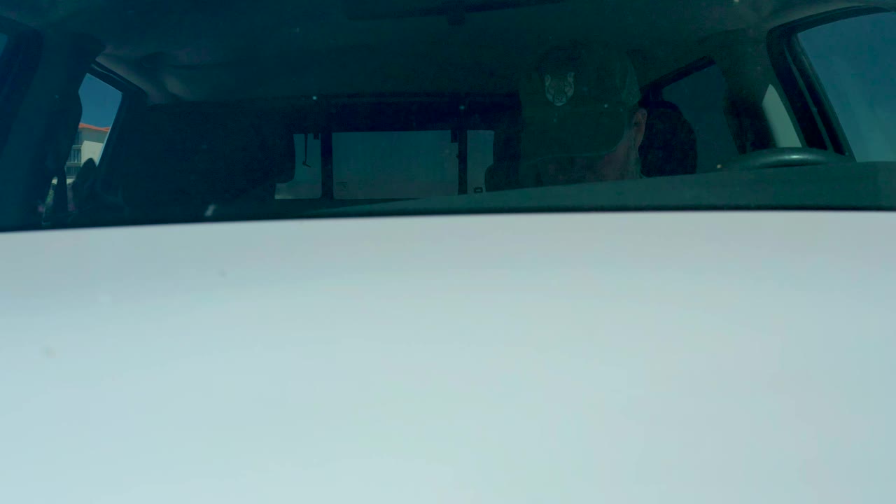 Front windshield view of the SUV at Dreams Los Cabos, with a shadowed cabin, indistinct occupants, and strong daylight washing across the lower glass.