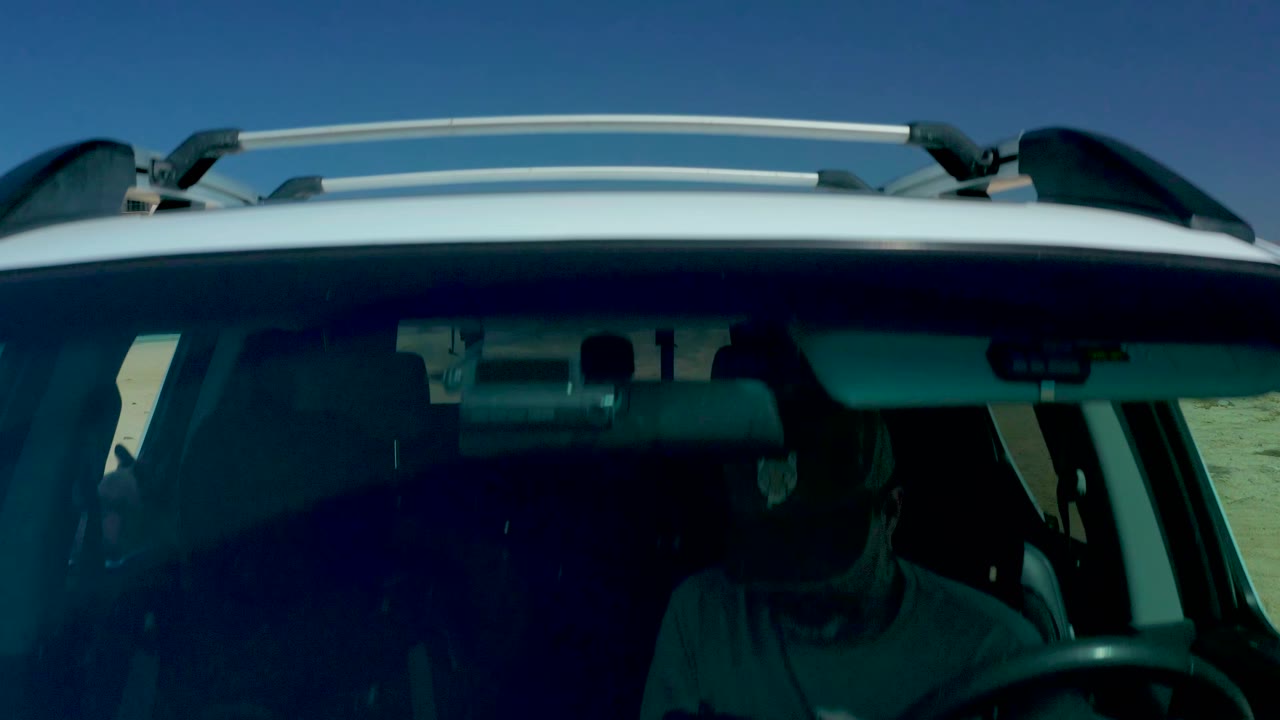 The SUV front and roof rack fill the lower frame at Dreams Los Cabos, with a driver silhouette visible behind the windshield and open blue sky above.