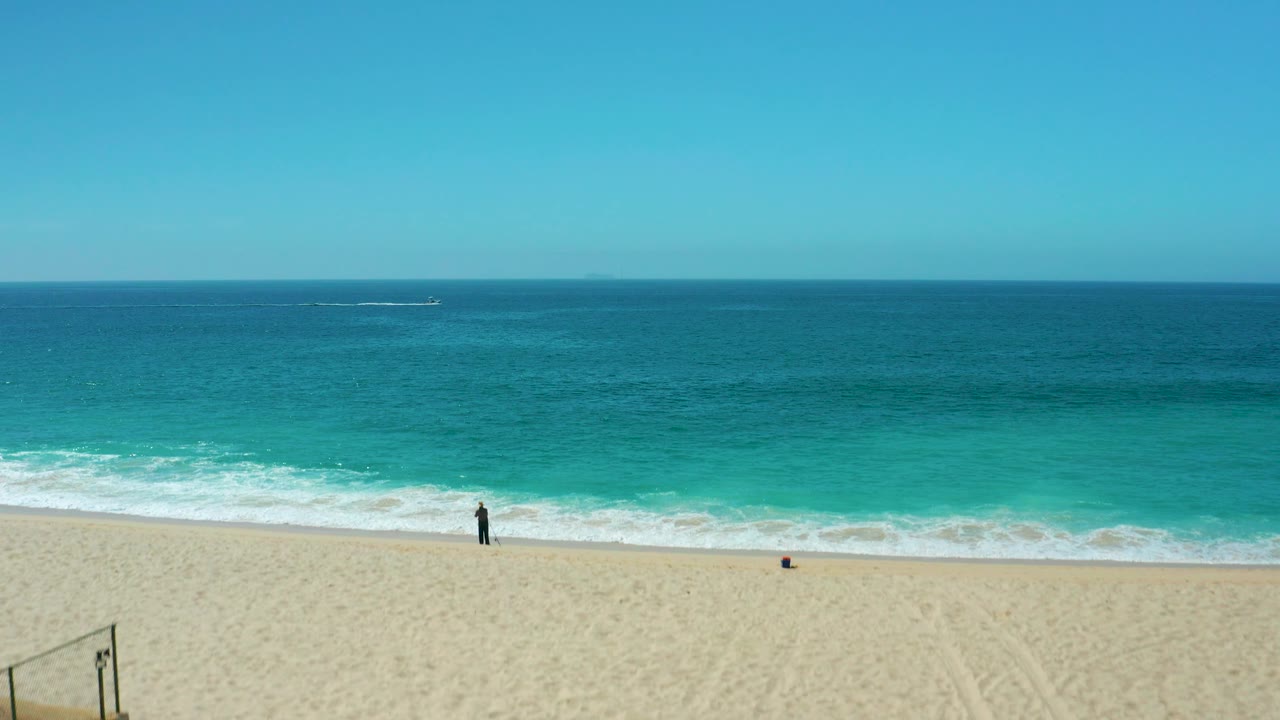 Shoreline view with sand at the bottom, turquoise waves, and a person near the water.