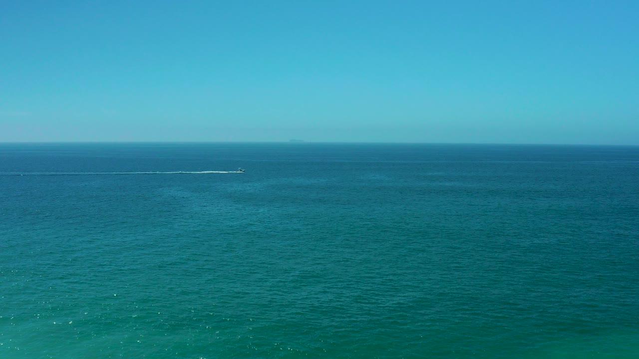 Wide blue ocean with a small boat wake near the horizon