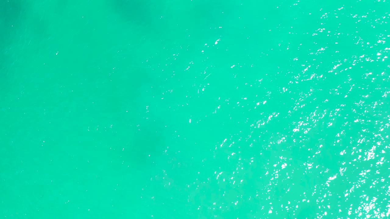 Clear teal ocean water at Dreams Los Cabos with a denser cluster of white sparkles across the surface and no visible people.