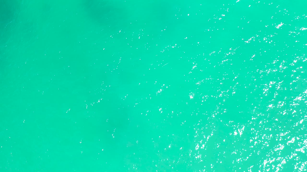Top-down turquoise ocean surface at Dreams Los Cabos with fine ripples, bright glints, and no visible people or objects.