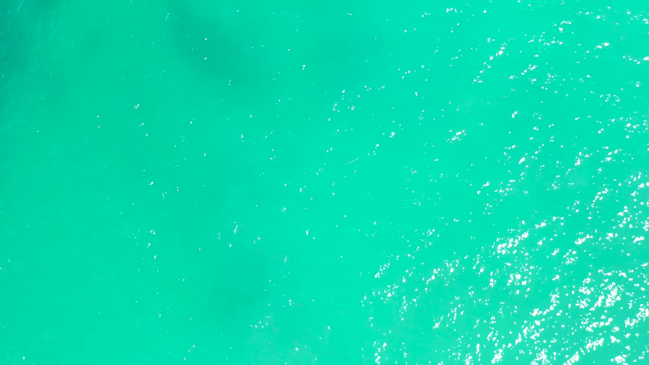 Bright aqua ocean surface at Dreams Los Cabos with scattered sunlight sparkles and soft darker shapes below the water, no visible people.