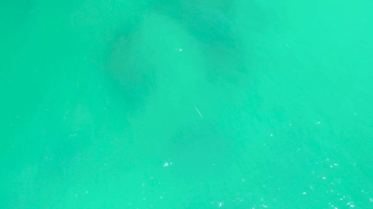 Overhead view of turquoise shallow water at Dreams Los Cabos, Baja California Sur, with faint darker seabed patches, small ripples, bright reflections, and no visible people.
