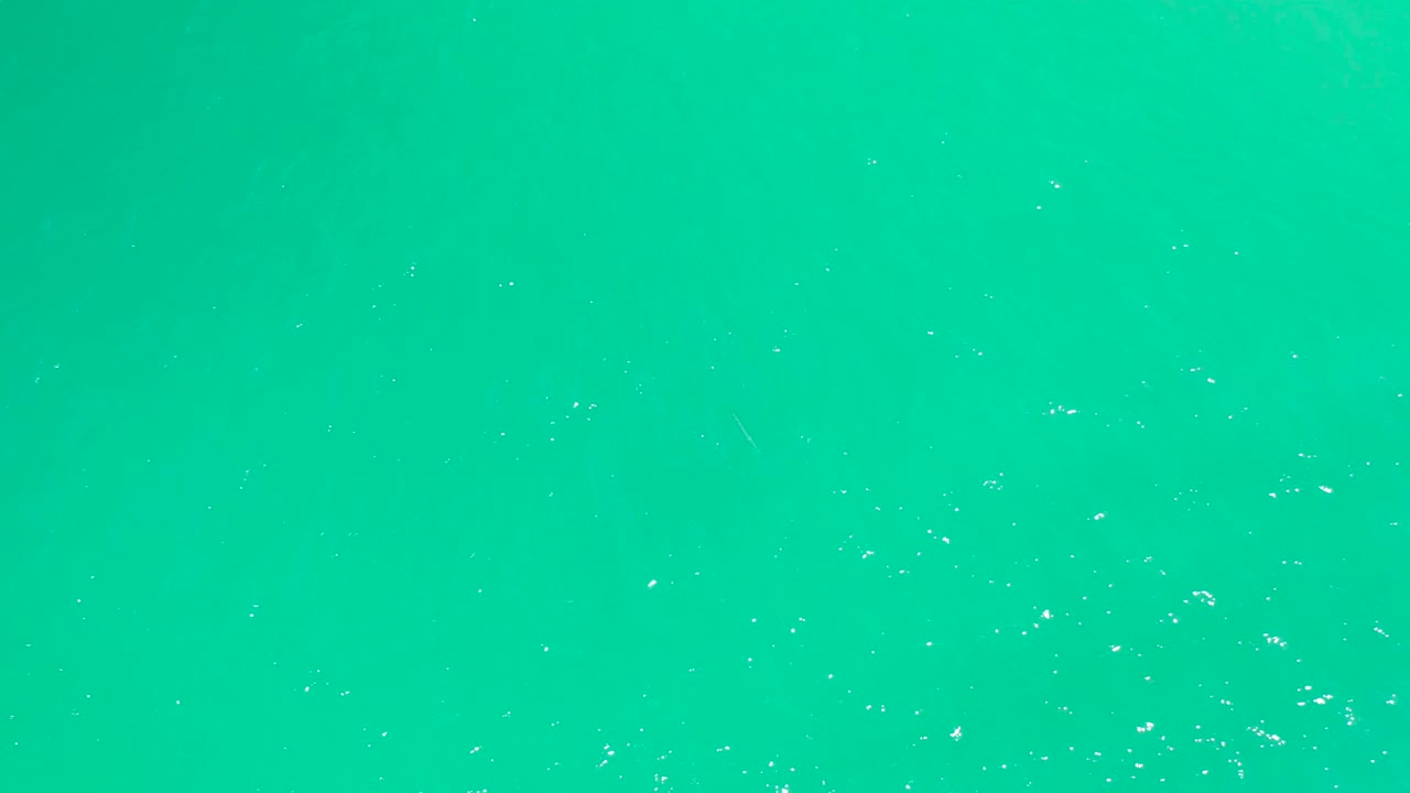 Overhead green turquoise water at Dreams Los Cabos with faint white bubbles and foam specks lightly dispersed across the surface, no visible people.