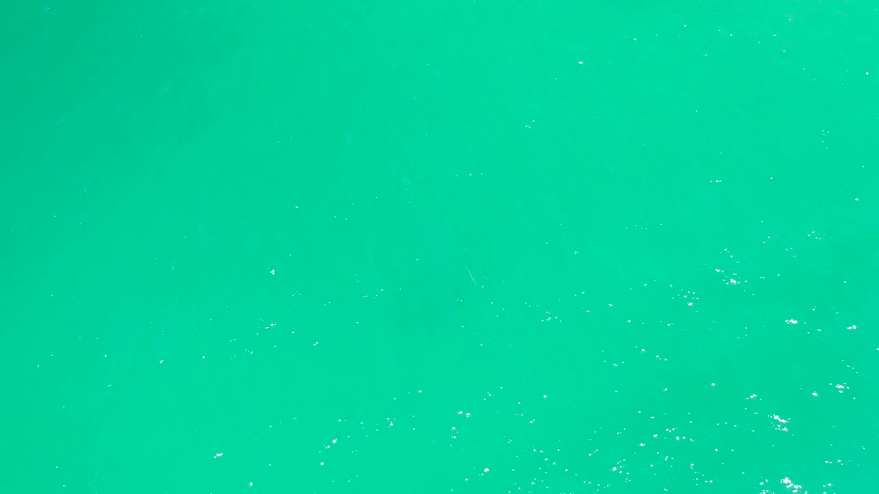 Top-down view of the Dreams Los Cabos ocean surface with small white foam clusters appearing more concentrated near the right side, no visible people.