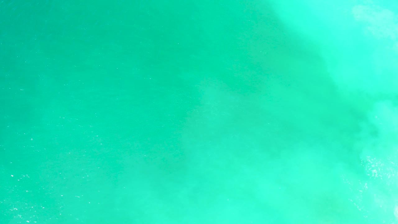 Turquoise ocean surface with pale white wash and a faint dark shape below.