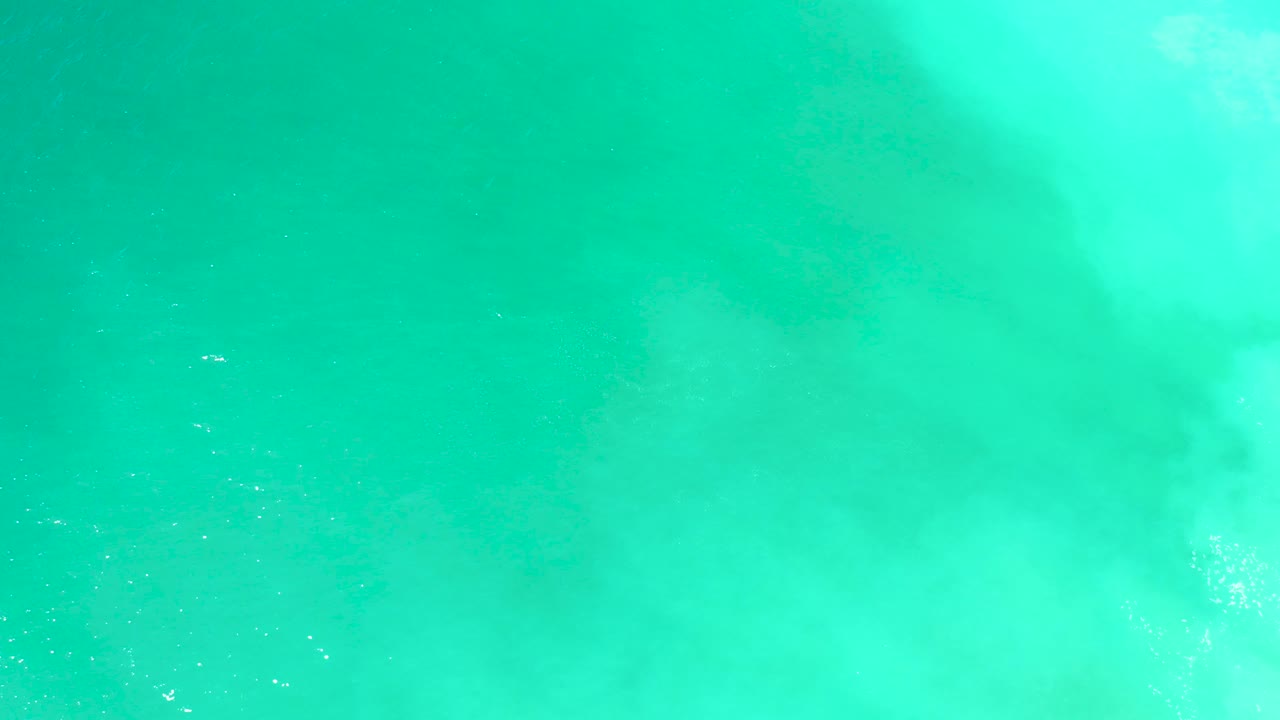 Midway through the clip, a larger dark shadow is visible below turquoise water at Dreams Los Cabos, partially covered by white surface streaks and with no visible people.