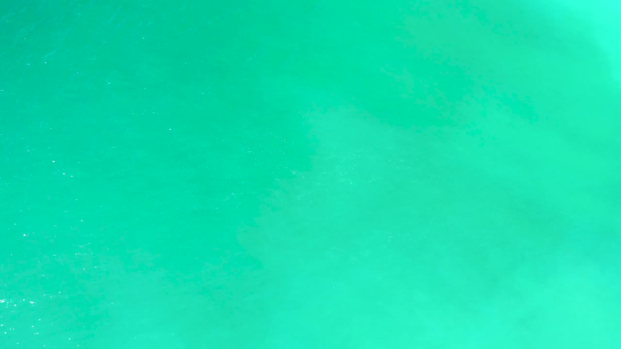 Clear blue-green ocean at Dreams Los Cabos shows soft foam traces across the surface with no visible people.
