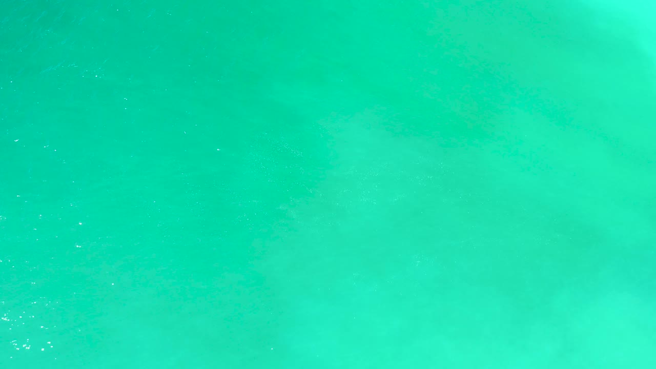 A top-down view at Dreams Los Cabos shows turquoise water with pale foam patches and no visible people or shoreline.
