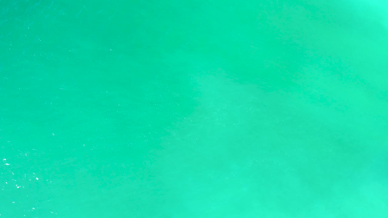 Calm turquoise ocean at Dreams Los Cabos fills the frame with scattered white foam specks and no visible people.