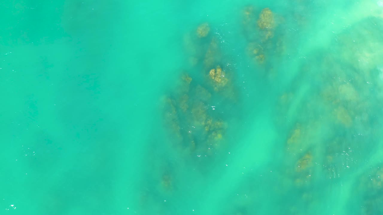 Clear aqua water at Dreams Los Cabos shows a dark seabed cluster slightly left of center with pale sandy areas around it and no visible people.