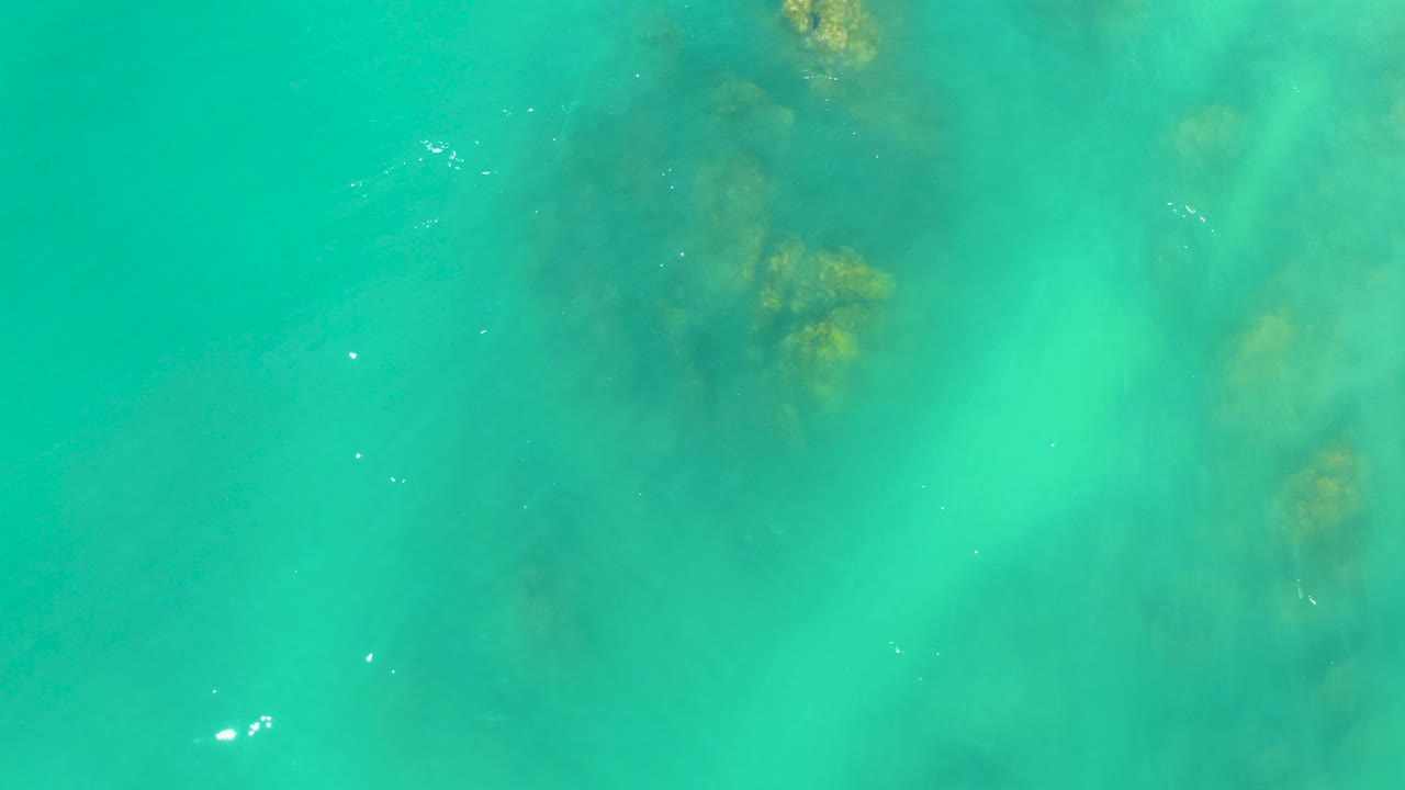 Top-down view of turquoise water over dark submerged rocks at Dreams Los Cabos, with faint pale clouding under the surface and no visible people.