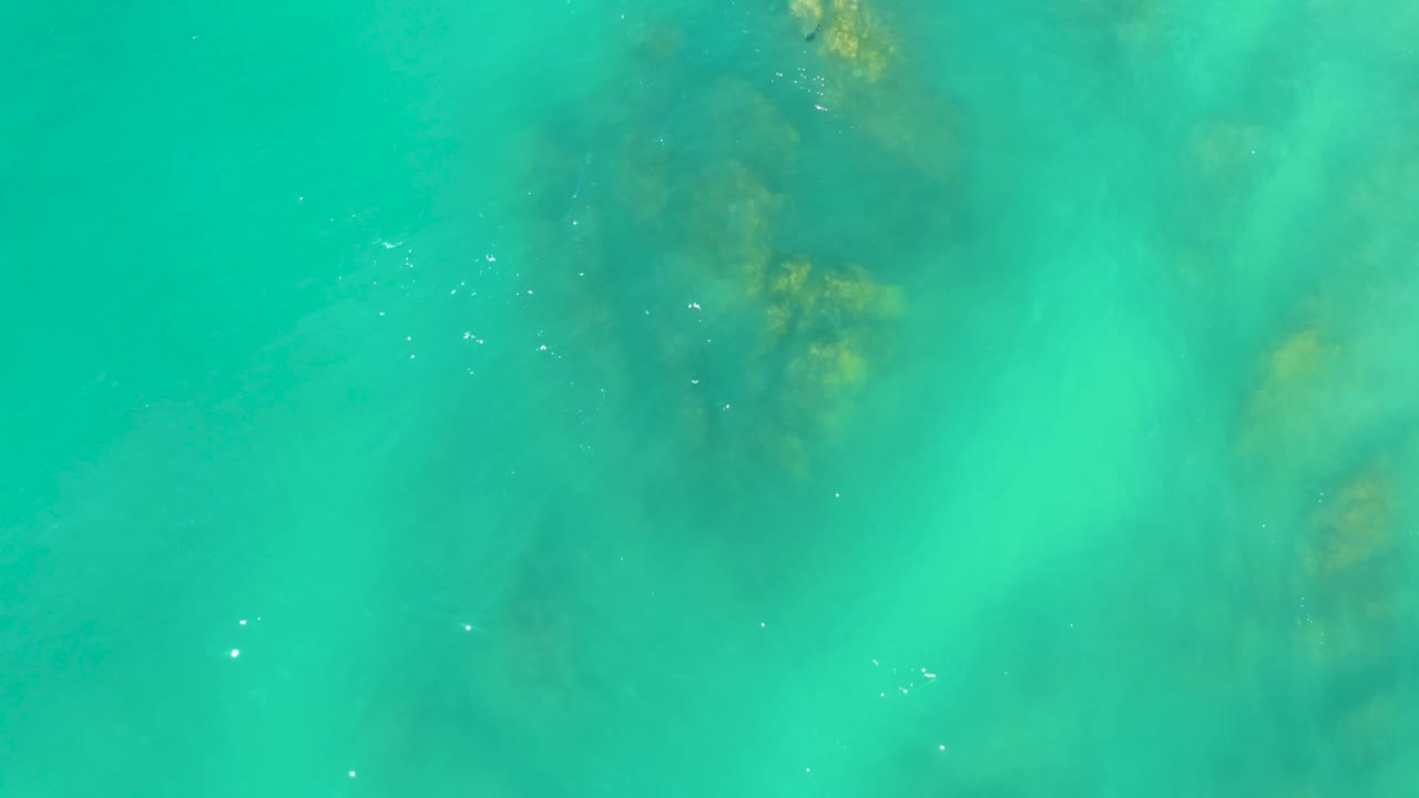 Ruffled turquoise water at Dreams Los Cabos passes over submerged rocks and yellow-brown underwater patches, with no shoreline or people visible.