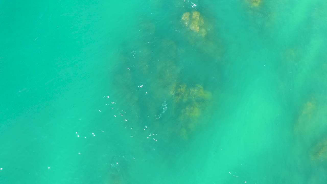 Overhead view at Dreams Los Cabos of clear turquoise water with muted submerged rocks near the upper frame and no visible people.