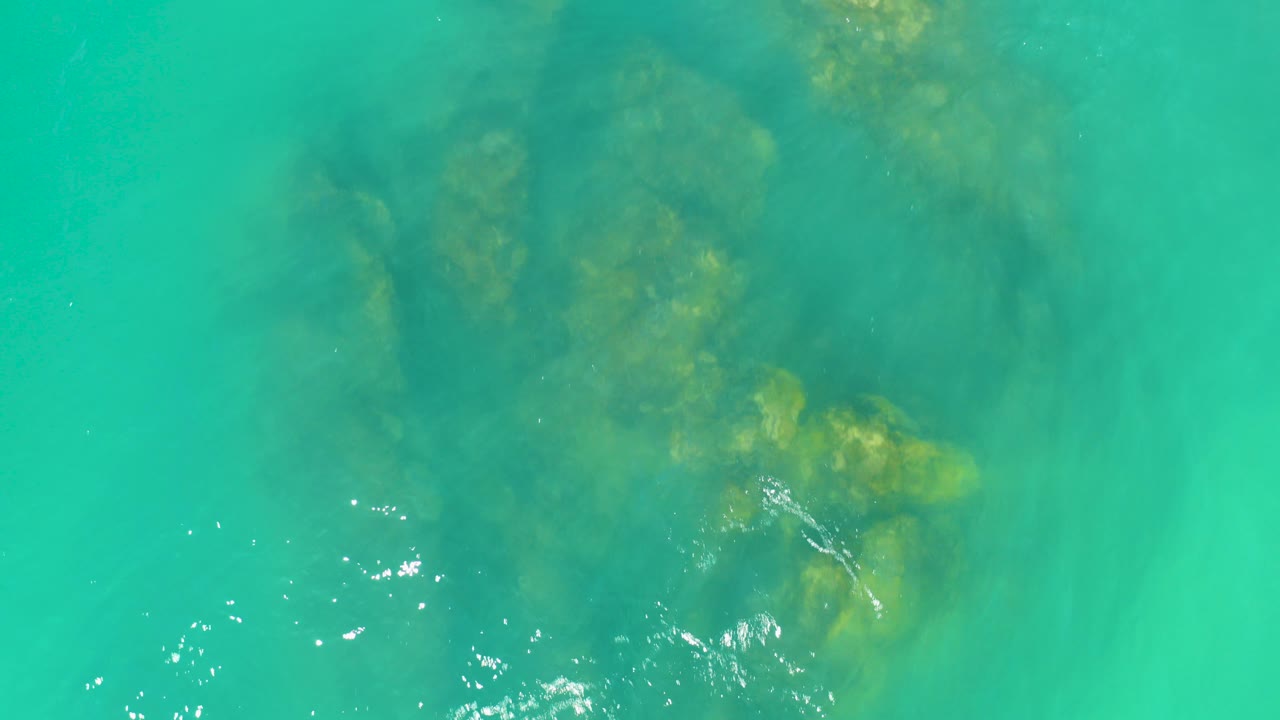 Turquoise water over submerged rocks with bright surface glints.