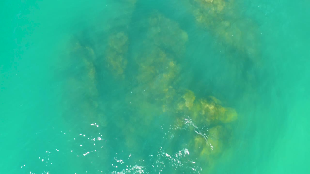 Clear green-blue water reveals a darker submerged rock patch near the upper center at Dreams Los Cabos, with no visible people.