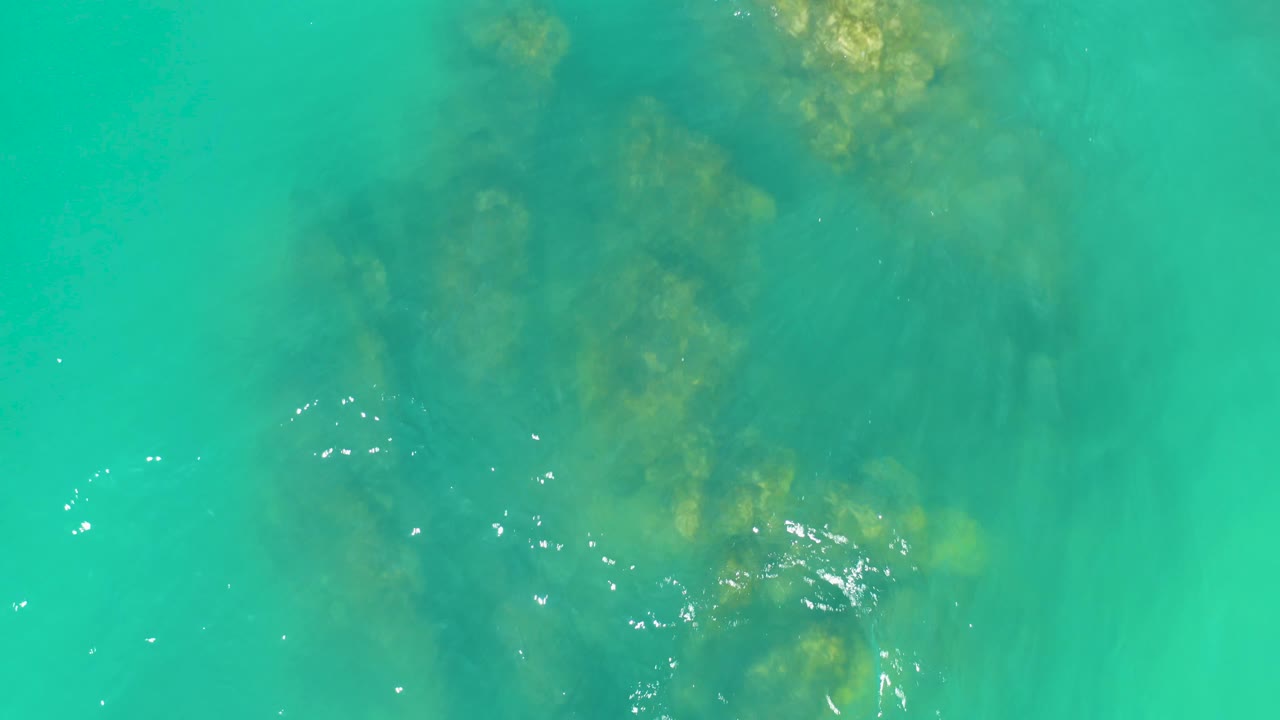 Turquoise ocean water at Dreams Los Cabos shows broken submerged rock forms under small white ripple highlights, with no visible people.