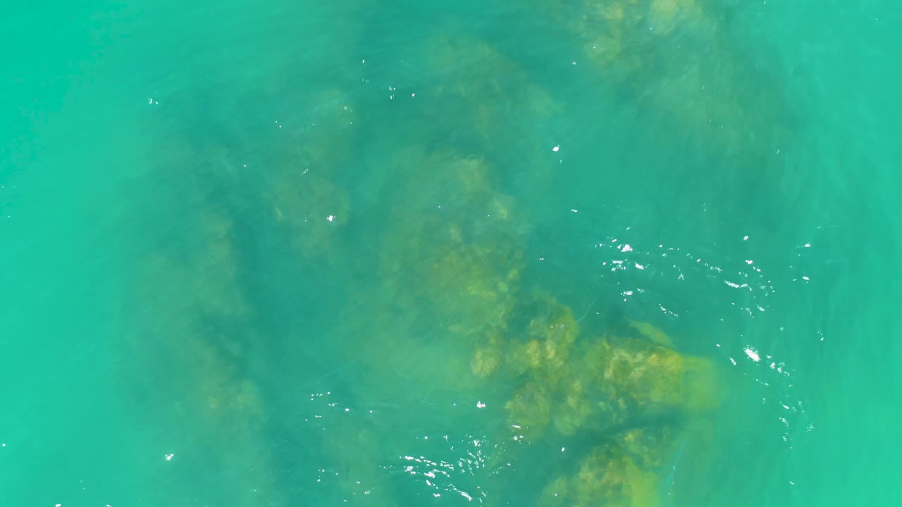 Turquoise ocean surface at Dreams Los Cabos shows ripples and bright reflections shifting over submerged rock shapes, with no visible people.