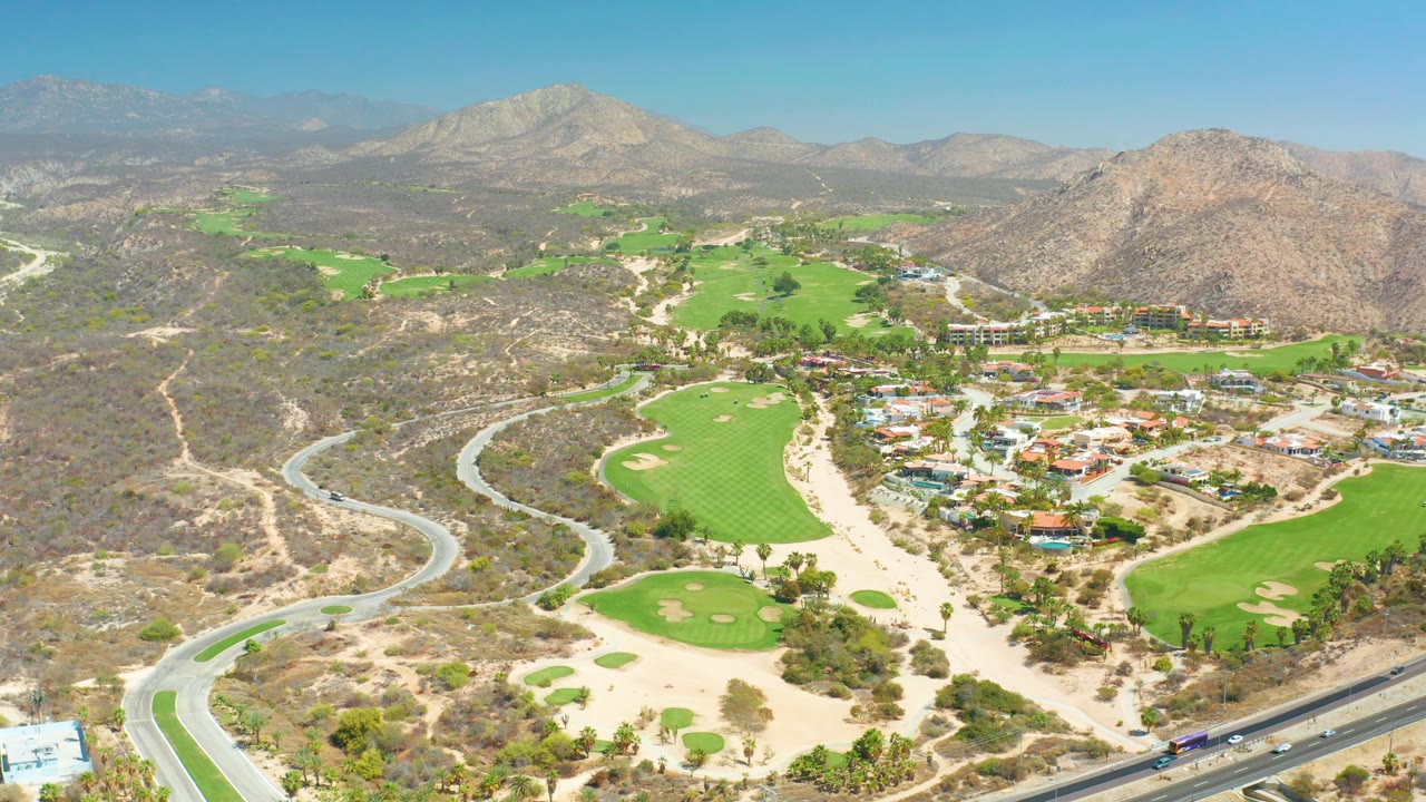 Drone-style aerial view of a golf course beside dry hills and winding roads.