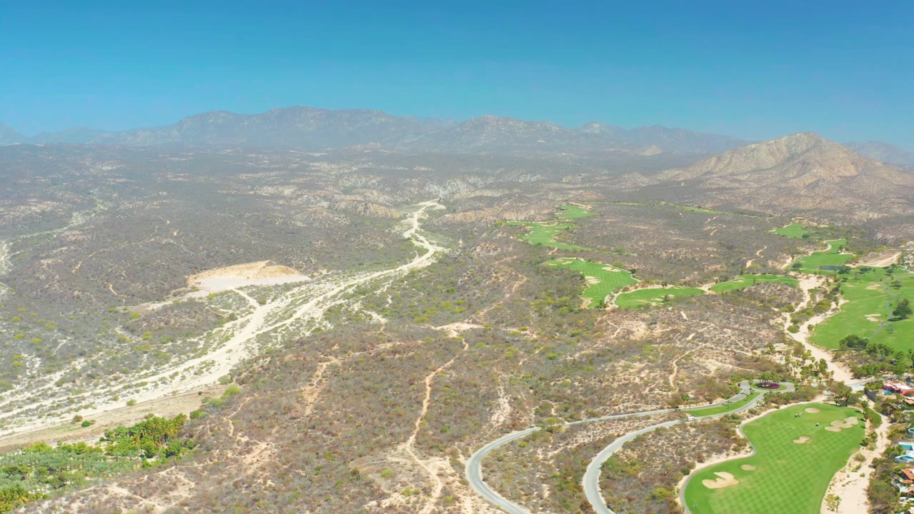 Golf course greens and sand traps sit beside pale roads in dry mountain terrain.