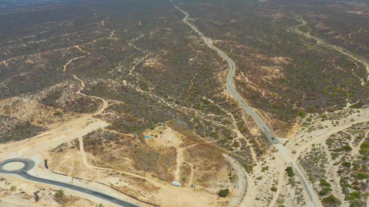 Opening aerial frame near Dreams Los Cabos shows winding desert roads, tan dirt cuts, scattered scrub, and tiny vehicles with no visible people.