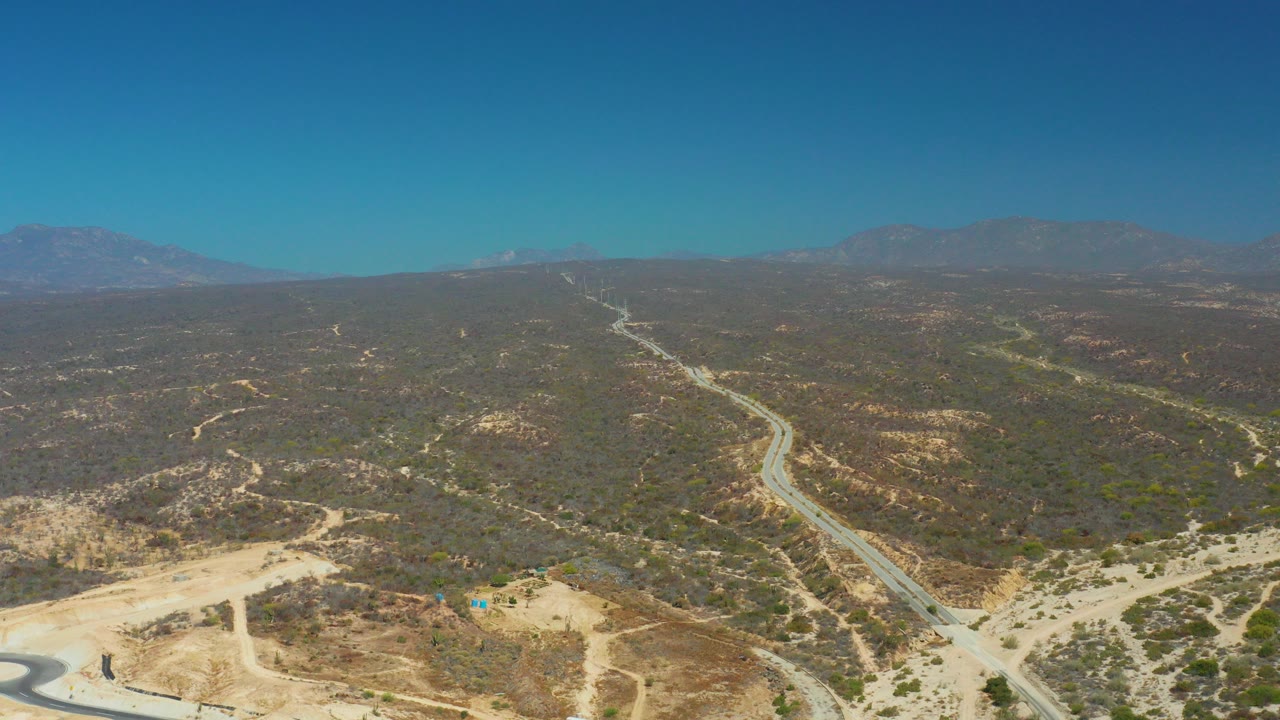Aerial view at Dreams Los Cabos in Baja California Sur showing winding roads across dry hills, distant mountains, clear blue sky, and no visible people.
