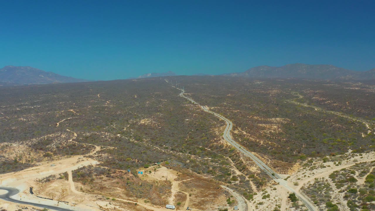 Aerial road scene across dry hills with mountains on the horizon.