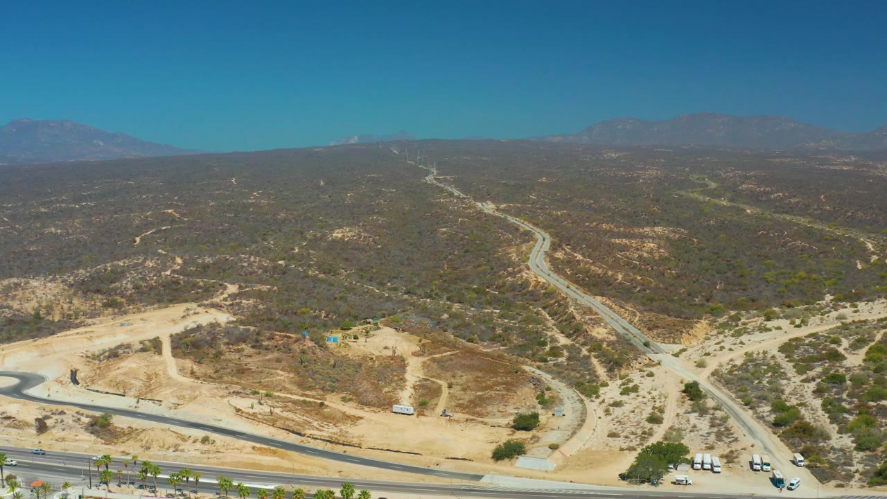 Highway and parking lot edge below dry hills and a winding road.