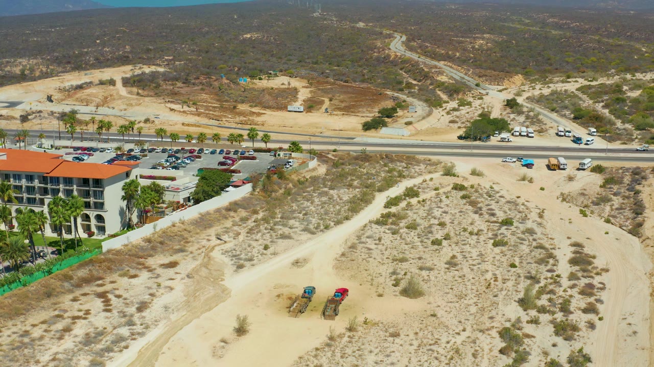 Aerial view of red-roofed building beside palms, road, and sandy hillside.