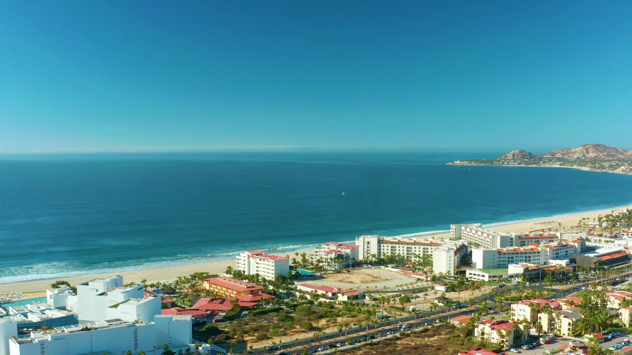 High view across beachfront development toward blue ocean and distant hills.