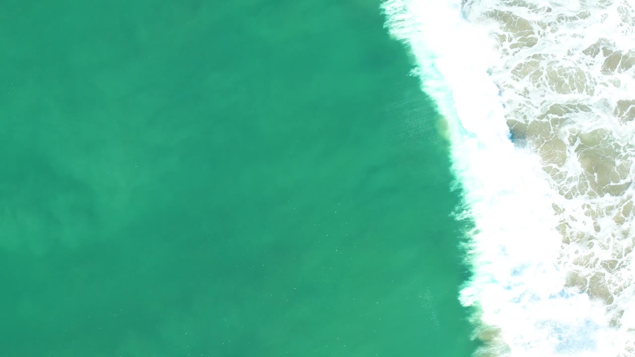 Open turquoise water sits beside dense white shoreline foam along the right edge of an overhead San Jose Del Cabo ocean view, with no visible people.