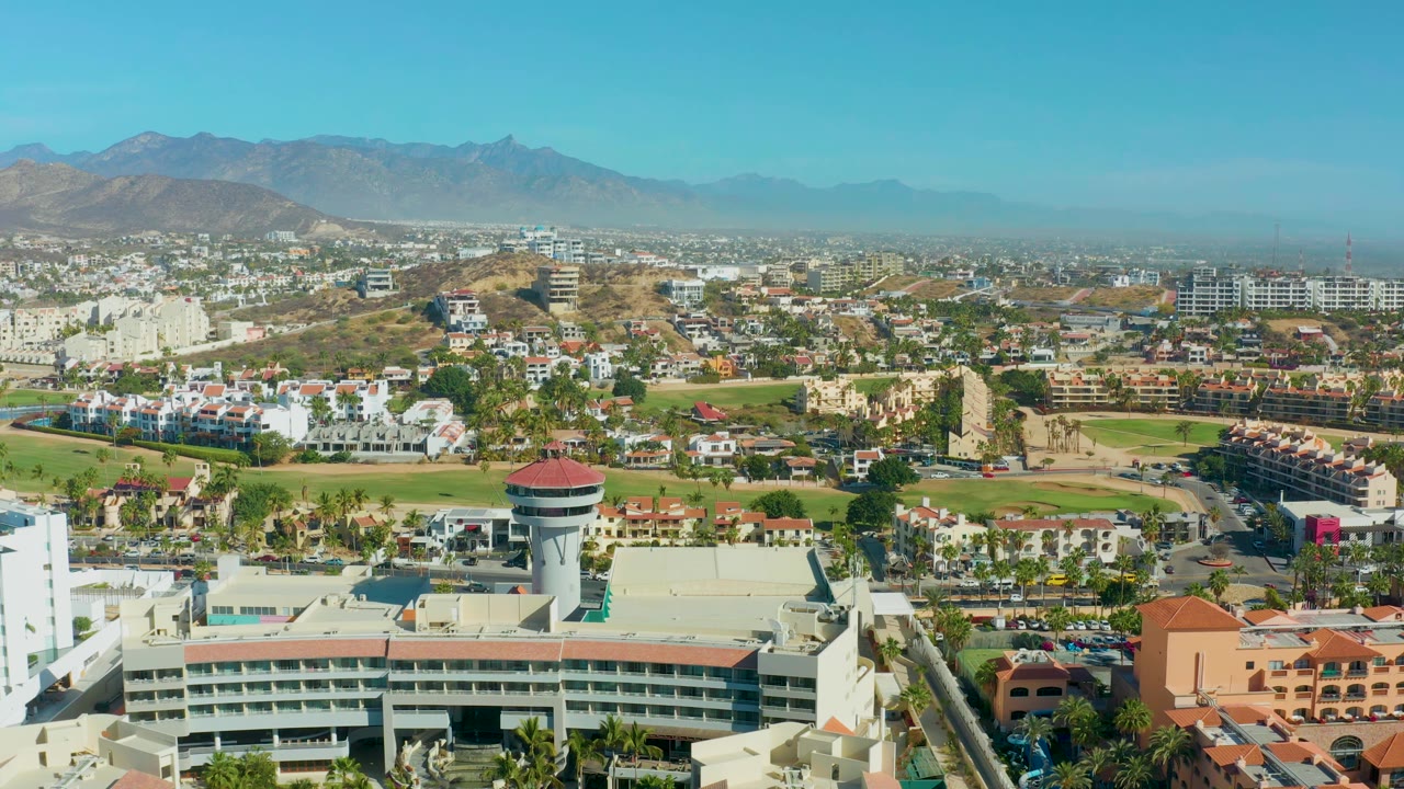 Panning aerial view over city buildings and water tower beneath mountains
