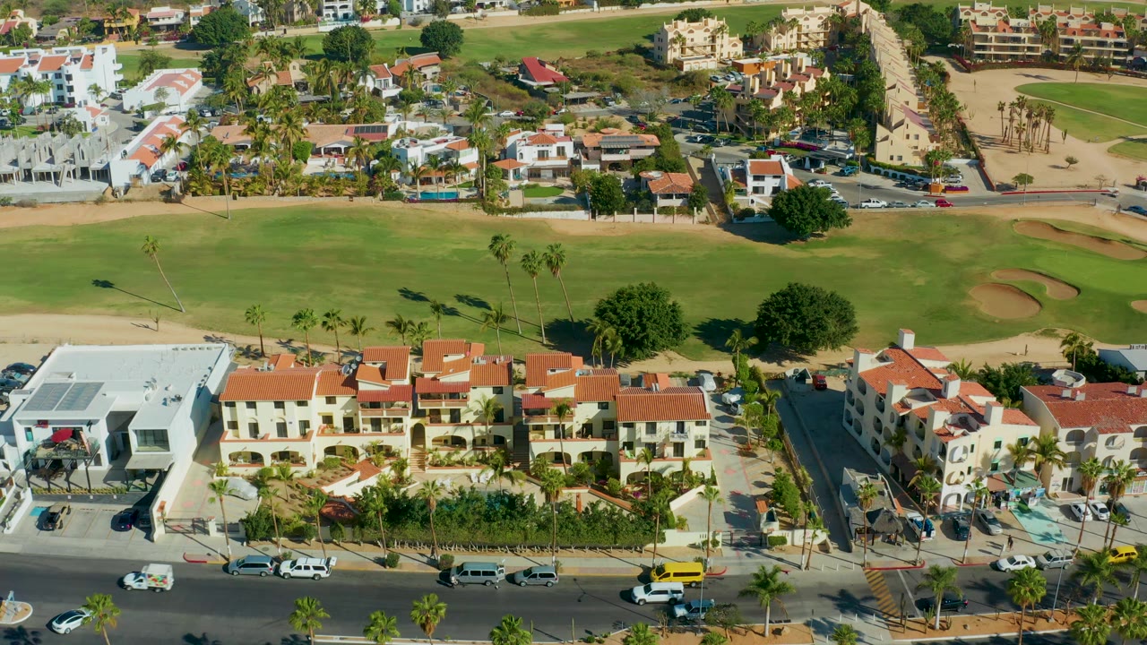 Overhead view of homes, road traffic, palms, and golf grass