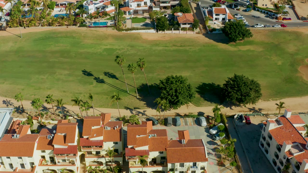 Golf course fairway with palm trees and red roof buildings along the bottom edge