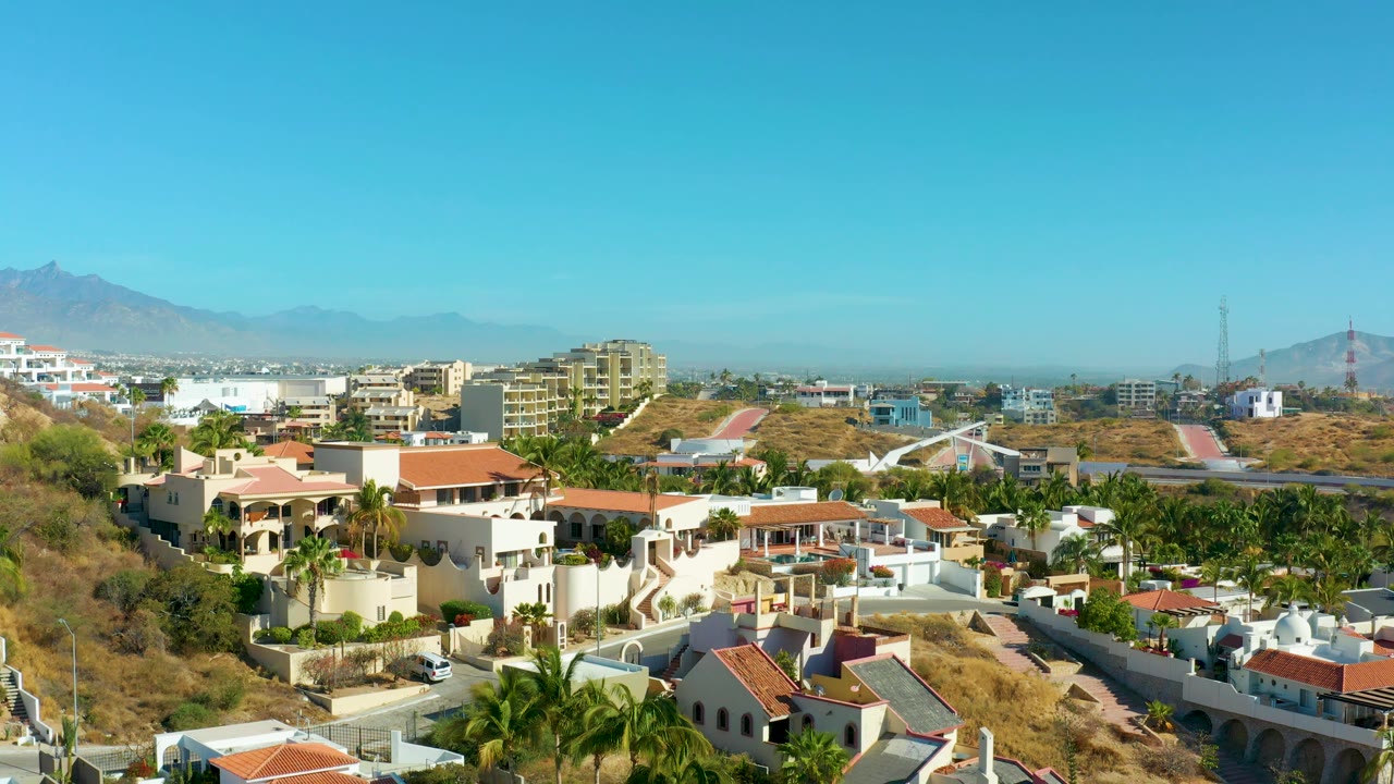 Hillside neighborhood with villas, dry terrain, and mountains.