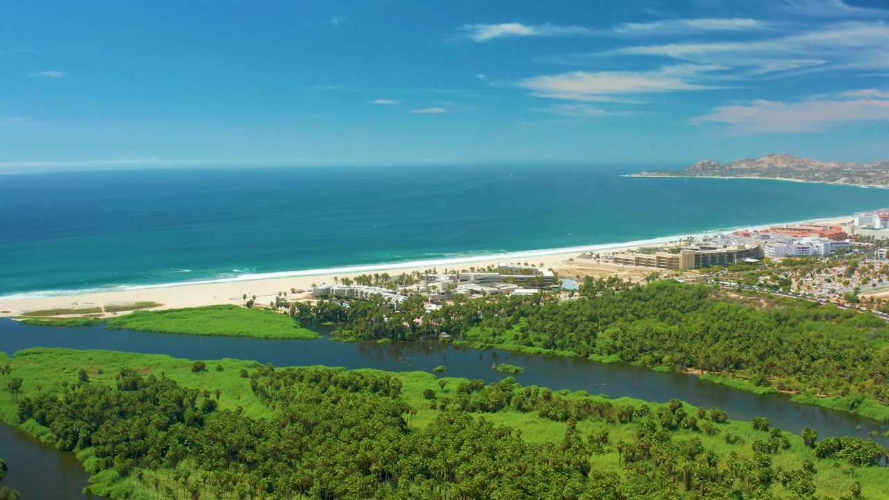 Aerial coastal panorama with river, trees, beach, ocean, and distant land.