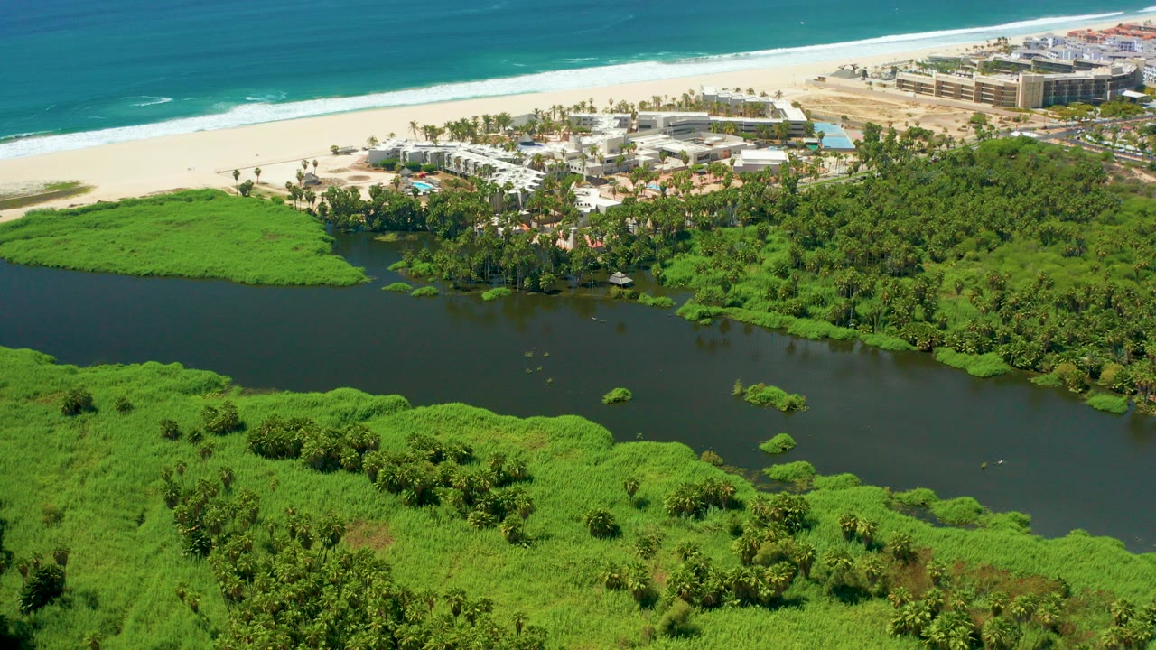 Aerial view of river, green wetlands, beach buildings, sand, and ocean.