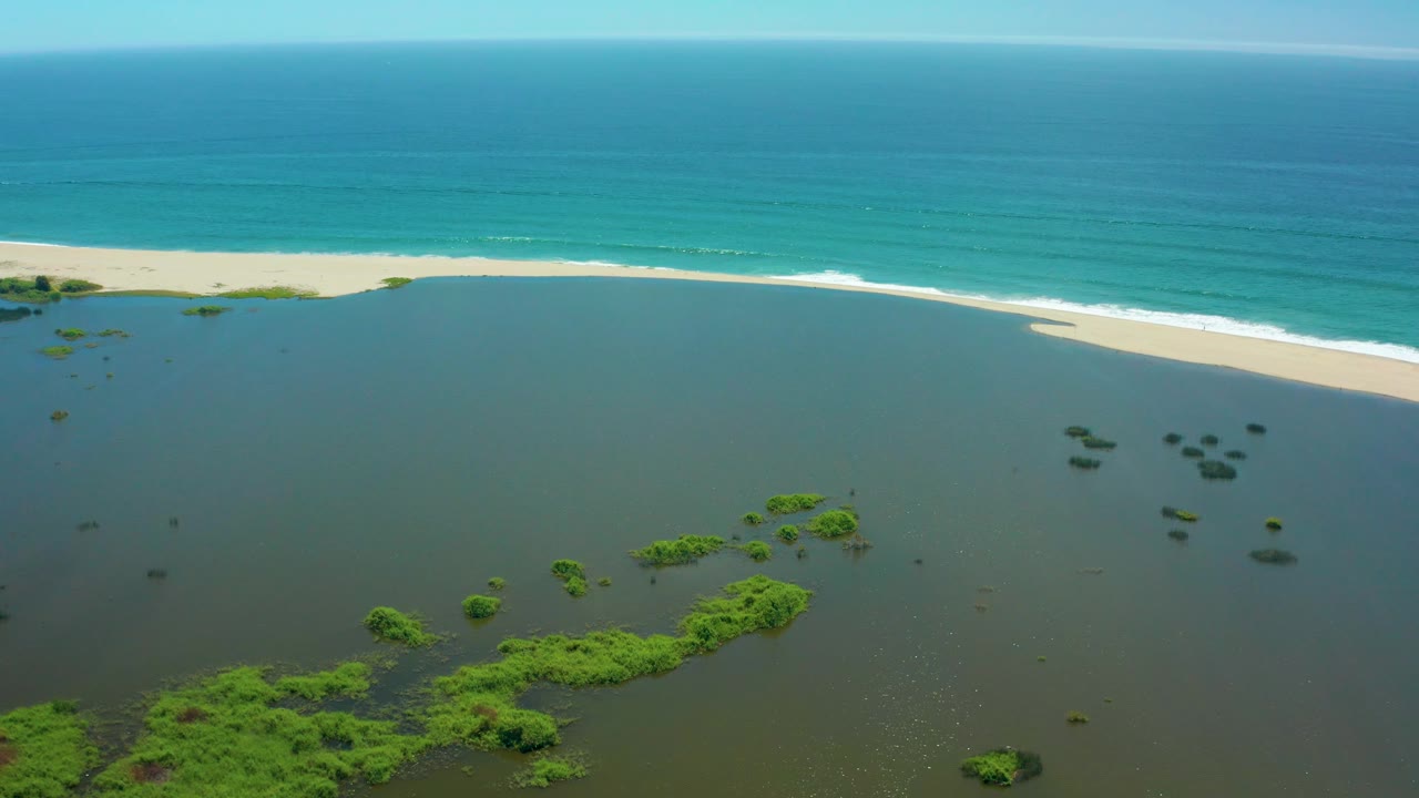 Coastal lagoon and beach with turquoise ocean under clear sky.