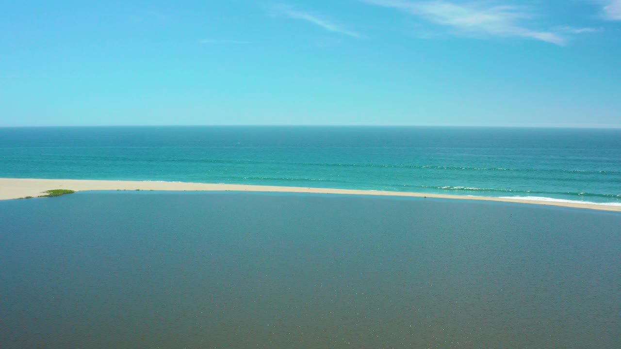 Aerial view of lagoon water, sandbar, ocean surf, and blue sky.