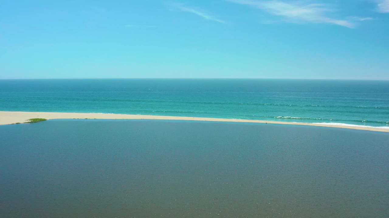 San Jose del Cabo shoreline frame with the sandbar running horizontally, small white wave lines offshore, clear sky, and no visible people.