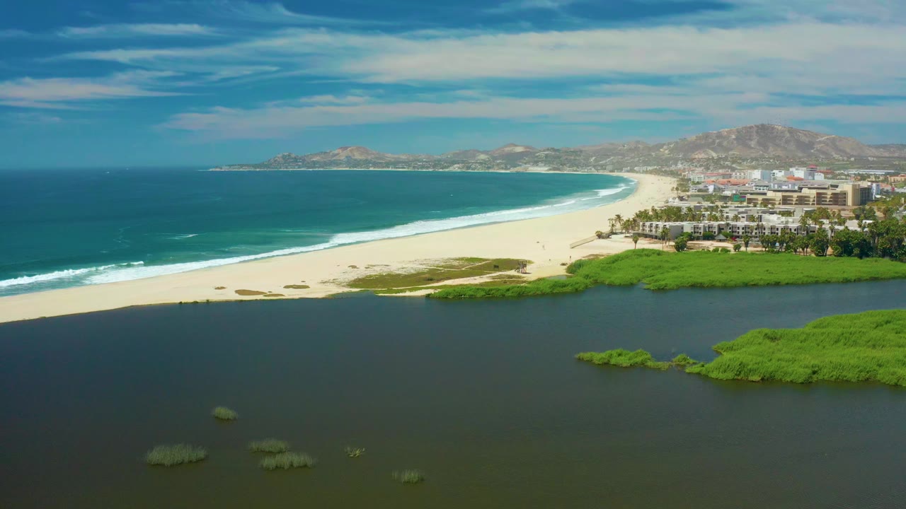 Aerial view of lagoon, mangroves, beach, ocean, buildings, and hills.